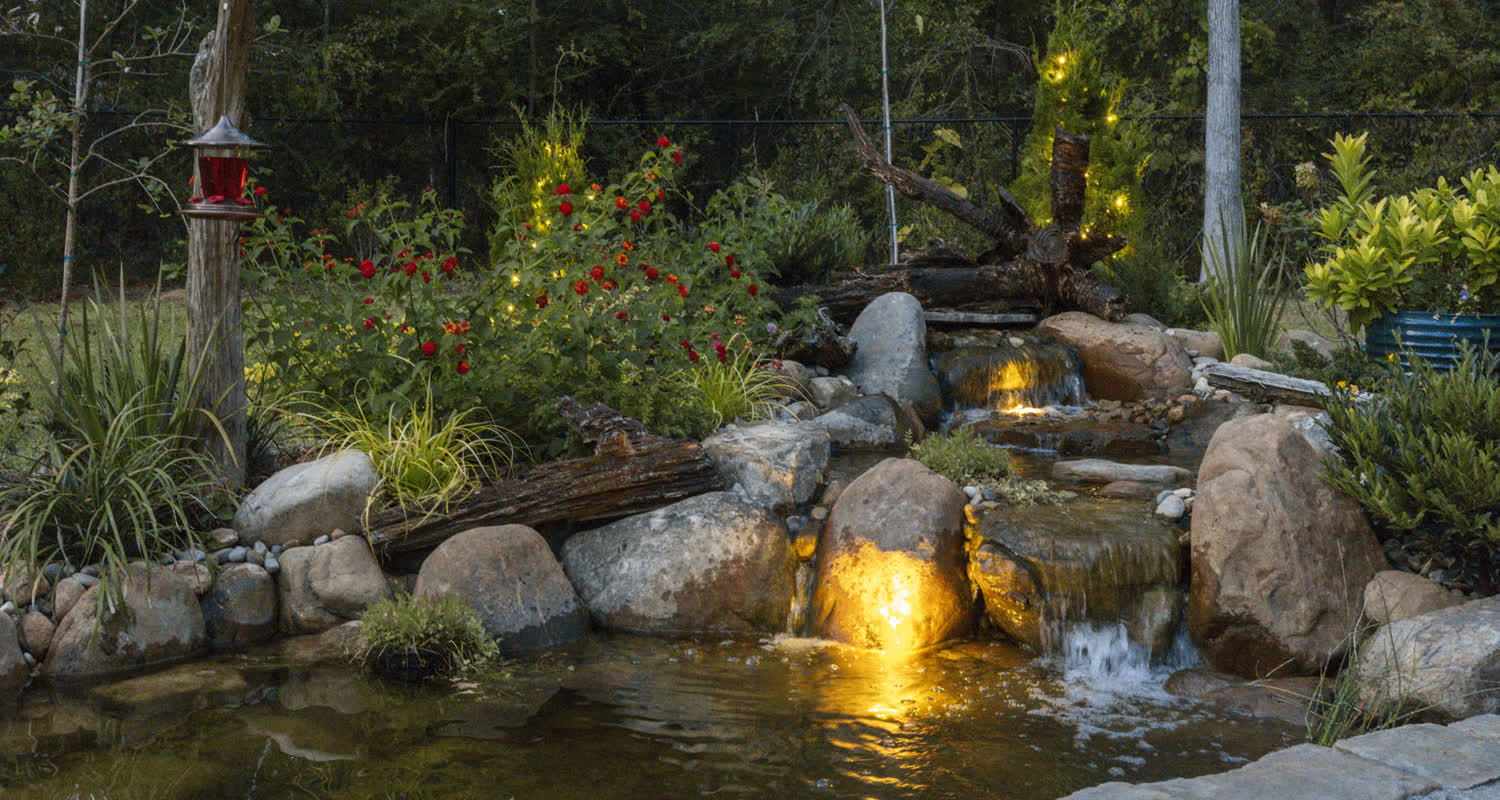 A Superscapes pondless waterfall lit at dusk