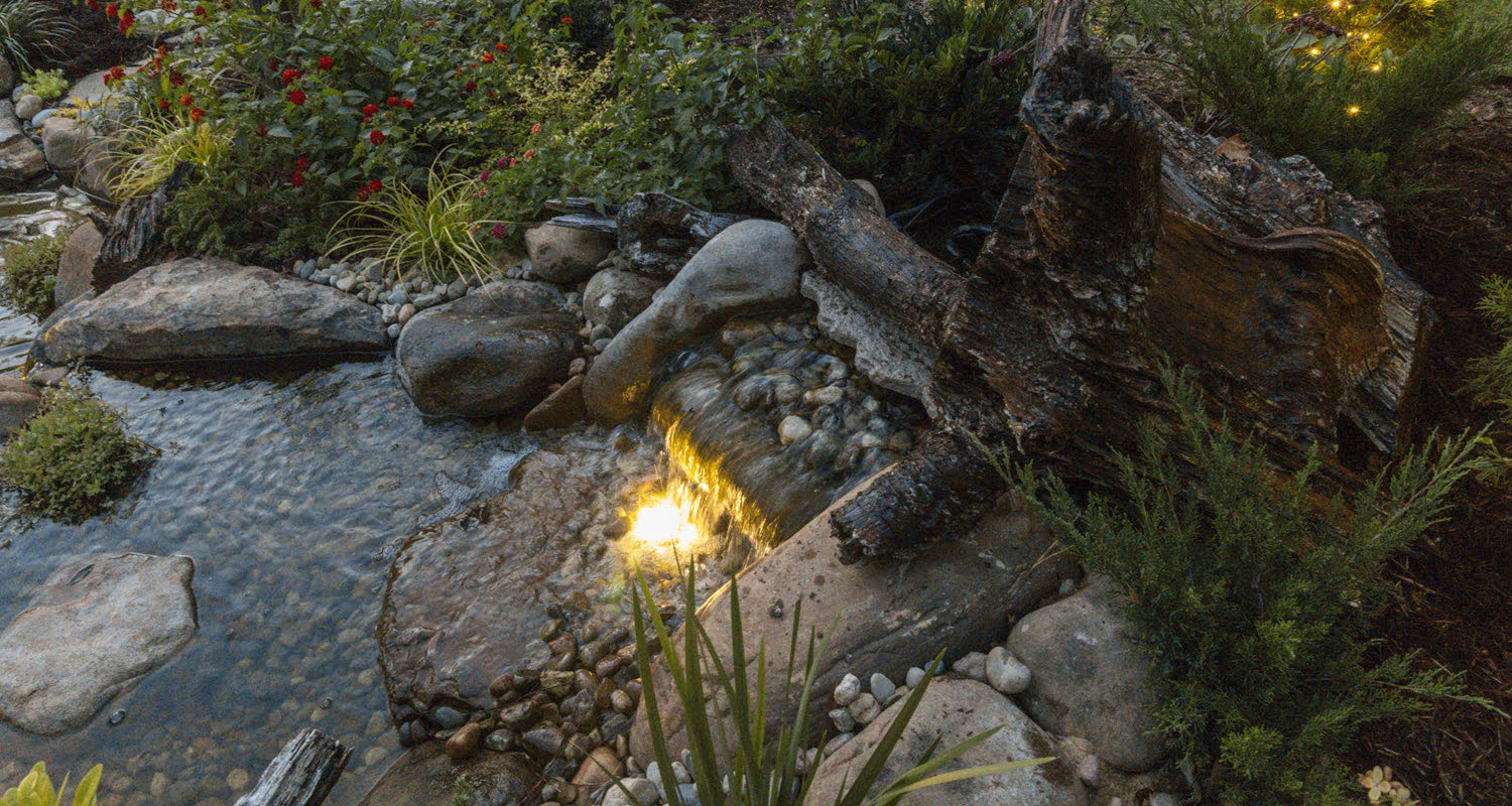 A Superscapes pondless waterfall set into a planted, lit garden at dusk